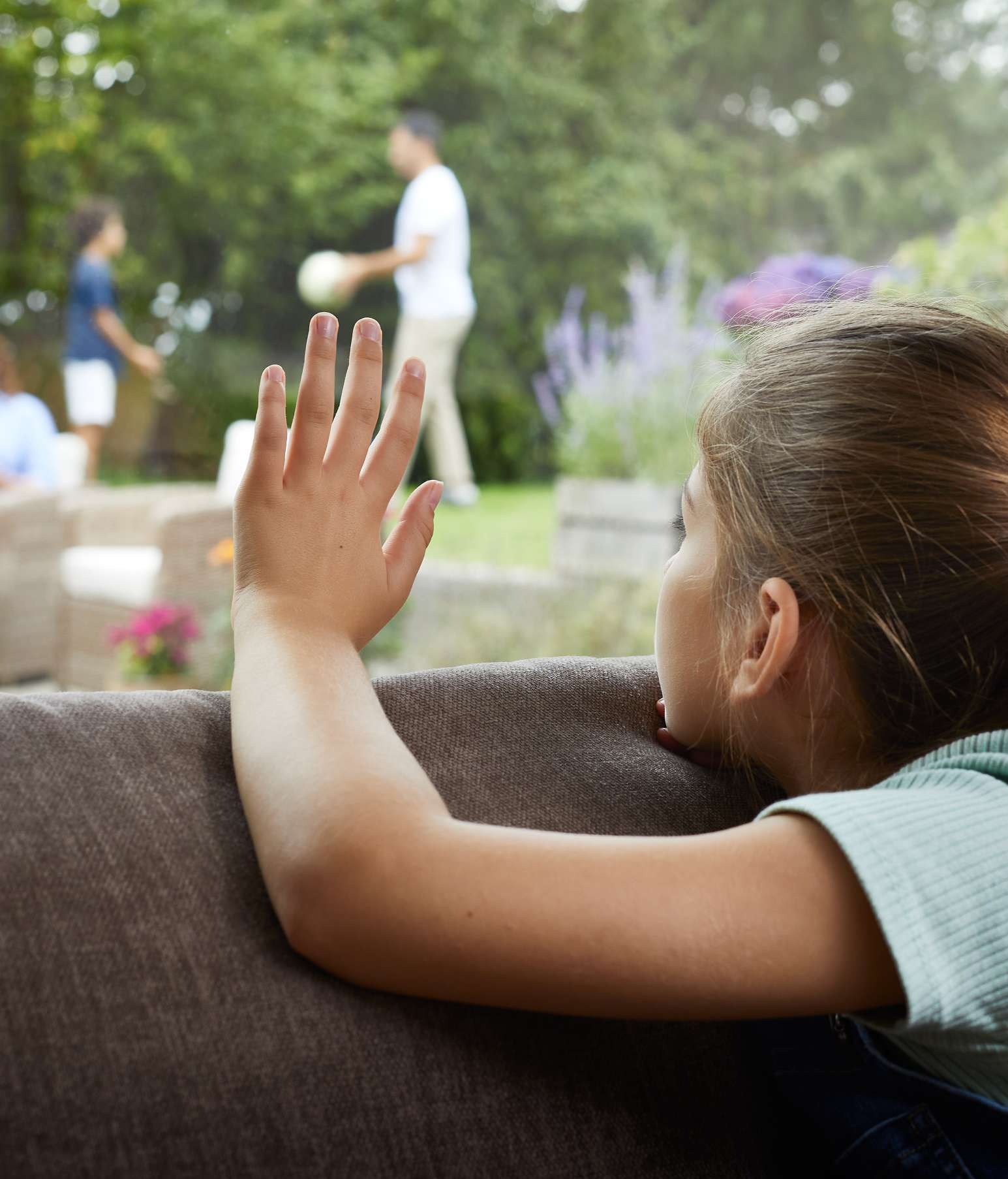 En pige sidder i en sofa og kigger ud ad vinduet, mens hun vinker til sin familie. Pollenallergi kan betyde, at børn må holde sig indenfor på dage med høje pollental.