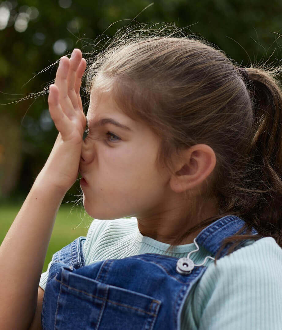 En pige i denimkjole gnider håndfladen mod næsen. Kløe i næsen er et almindeligt symptom på pollenallergi.