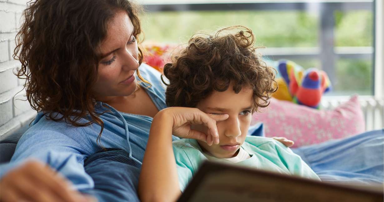 En mor og hendes søn sidder i en sofa og læser. Drengen klør sig i øjnene, hvilket er et almindeligt symptom på pollenallergi.